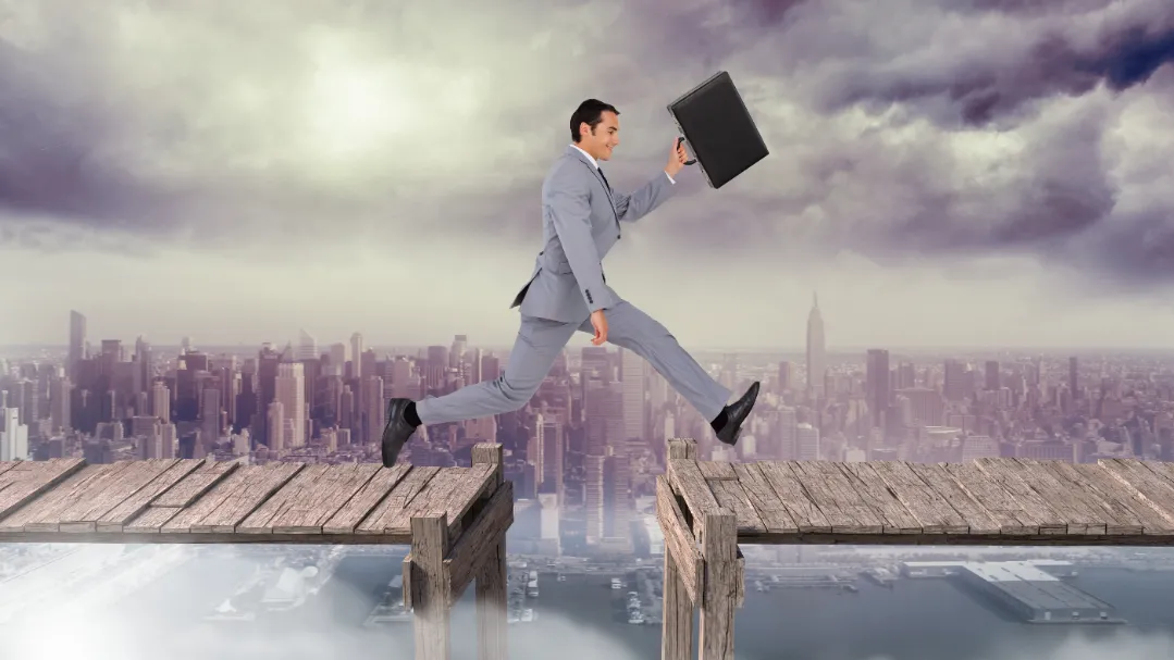A business professional in a suit leaps over a broken bridge between two platforms high above a city skyline, symbolizing overcoming gaps and challenges in recruitment vendor partnerships.
