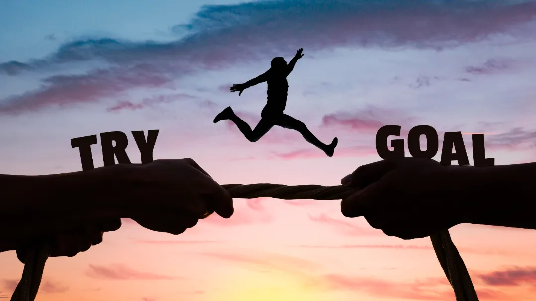 Silhouette of a person leaping from the word “TRY” to “GOAL” at sunset, symbolizing overcoming challenges and achieving success in recruitment vendor collaboration.