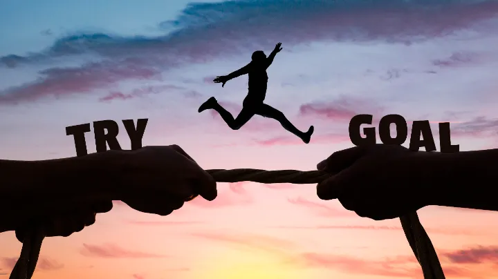Silhouette of a person leaping from the word “TRY” to “GOAL” at sunset, symbolizing overcoming challenges and achieving success in recruitment vendor collaboration.